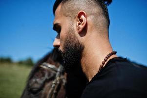 l'uomo arabo con barba alta indossa in nero con cavallo arabo. foto