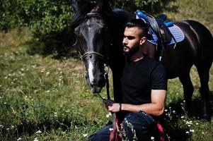 l'uomo arabo con barba alta indossa in nero con cavallo arabo. foto