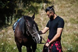 l'uomo arabo con barba alta indossa in nero con cavallo arabo. foto