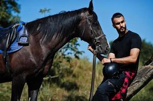 l'uomo arabo con barba alta indossa in nero con cavallo arabo. foto