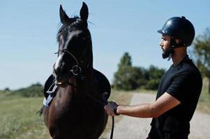 l'uomo arabo con barba alta indossa l'elmo nero con cavallo arabo. foto