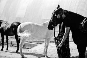 l'uomo arabo con barba alta indossa l'elmo nero con cavallo arabo. foto