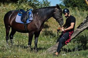 l'uomo arabo con barba alta indossa l'elmo nero con cavallo arabo. foto