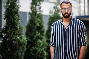 indossare uomo arabo di successo in camicia a righe e occhiali da sole posa all'aperto. foto