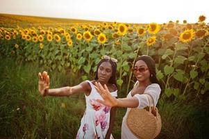 due piuttosto giovani amici neri donna indossano abiti estivi posano in un campo di girasoli. foto