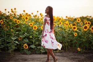 piuttosto giovane donna nera indossare abito estivo posa in un campo di girasoli. foto