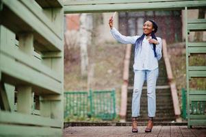 ragazza afroamericana alla moda con dreadlocks che tiene il telefono cellulare a portata di mano, tempo nevoso all'aperto. foto