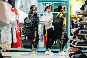 tre donne americane in tute da ginnastica che fanno shopping con borse sportive al centro commerciale di abbigliamento sportivo contro gli scaffali. tema del negozio di sport. foto