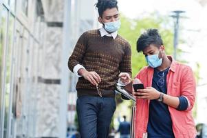 concetto di coronavirus covid-19. due uomini indiani del sud asiatico che indossano una maschera per proteggersi dal virus corona guardando il telefono cellulare. nuovo stile di vita normale post pandemia in India. foto