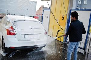 uomo del sud asiatico o maschio indiano che lava il suo trasporto bianco sull'autolavaggio. foto