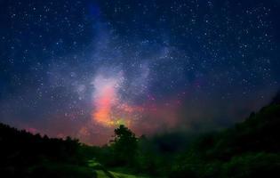 via lattea e luce rosa in montagna. paesaggio colorato notturno. cielo stellato con colline in estate. bellissimo universo. sfondo dello spazio con la galassia. sfondo di viaggio foto