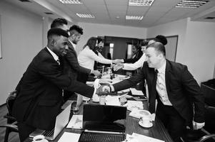 buon affare. team aziendale multirazziale che si rivolge alla riunione attorno al tavolo della sala riunioni e si stringe la mano a vicenda. foto