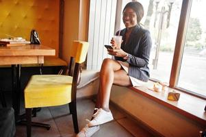 donna d'affari afroamericana che beve limonata cocktail nella caffetteria. ragazza nera che riposa con il telefono cellulare. foto