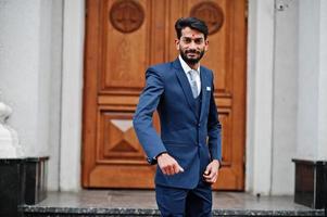 elegante barba uomo indiano con bindi sulla fronte, indossare su abito blu posato all'aperto contro la porta dell'edificio. foto