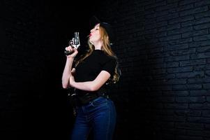 agente femminile dell'FBI in berretto e con la pistola in studio contro un muro di mattoni scuri. foto