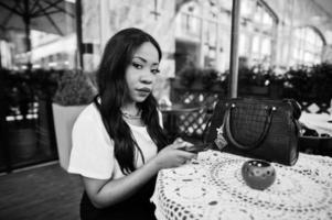 donna d'affari afroamericana alla moda che si siede al caffè all'aperto con il telefono cellulare. foto