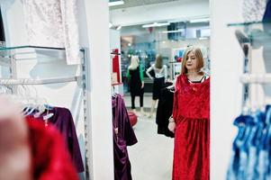 ragazza bionda prova un vestito rosso nella boutique, guardandosi allo specchio. foto