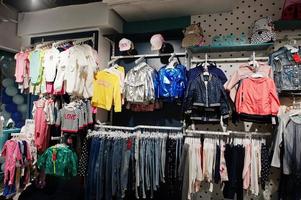 i vestiti luminosi per bambini sono appesi sul display nel negozio di abbigliamento per bambini. sezione ragazze. foto