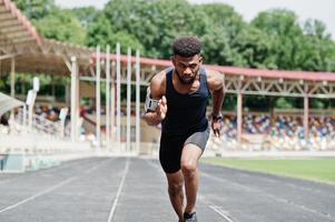 atleta maschio afroamericano in abbigliamento sportivo che corre da solo lungo una pista da corsa allo stadio.