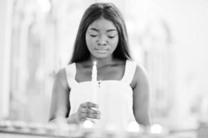 donna afroamericana che prega nella chiesa. i credenti meditano nella cattedrale e nel tempo spirituale della preghiera. ragazza afro con le candele. foto