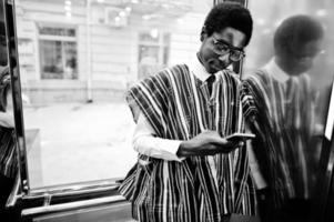 uomo africano in abiti tradizionali e occhiali con telefono cellulare a elavator o ascensore moderno. foto