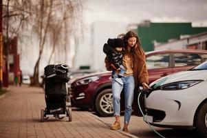 giovane madre con bambino che carica l'auto elettrica presso la stazione di servizio elettrica. foto