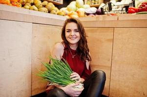 ragazza in rosso che tiene cipolle verdi sul negozio di frutta. foto