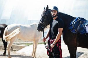 l'uomo arabo con barba alta indossa l'elmo nero con cavallo arabo. foto