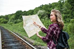 ritratto di una bella ragazza bionda in camicia scozzese che cammina sulla ferrovia con la mappa nelle sue mani. foto