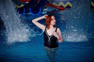 ragazza dai capelli rossi sexy in costume da bagno nero che riposa nella piscina del parco acquatico. foto