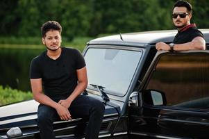 due fratelli asiatici indossano un uomo tutto nero in posa vicino a un'auto suv. foto