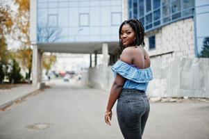 attraente donna afroamericana con dreadlocks in jeans indossano poste contro un moderno edificio a più piani. foto