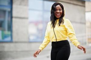 hipster ragazza afroamericana che indossa una felpa con cappuccio gialla in posa in strada. foto