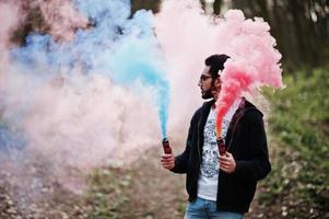 l'uomo arabo di street style con gli occhiali tiene il bagliore della mano con una bomba fumogena rossa e blu. foto