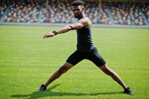 atleta maschio afroamericano in abbigliamento sportivo che fa esercizio di stretching allo stadio.