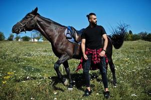 l'uomo arabo con barba alta indossa in nero con cavallo arabo. foto