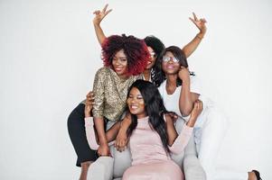 felici momenti positivi luminosi di quattro ragazze africane. divertirsi e sorridere sulla sedia contro il muro bianco vuoto. bei momenti di quattro migliori amici che si abbracciano. foto