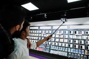 due indiani equipaggiano l'acquirente del cliente al telefono cellulare che fanno selfie con il bastone monopiede. concetto di popoli e tecnologie dell'Asia meridionale. negozio di cellulari. foto