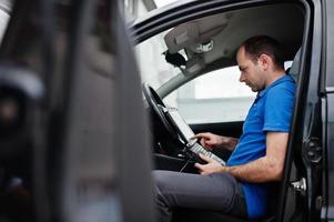 tema riparazione e manutenzione auto. meccanico elettrico in uniforme che lavora nel servizio auto, effettuando la diagnostica dell'auto utilizzando il dispositivo obd con il laptop. foto