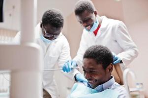 paziente uomo afroamericano in poltrona odontoiatrica. studio dentistico e concetto di pratica medica. risate sul posto di lavoro. perforazione dei denti del paziente in clinica. foto