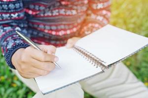 primo piano mano giovane uomo è seduto utilizzando penna scrittura record lezione blocco note nel libro sul tavolo in legno. foto