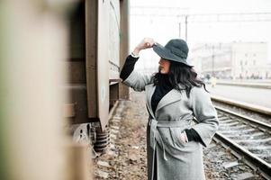 ragazza bruna in cappotto grigio con cappello in stazione ferroviaria. foto