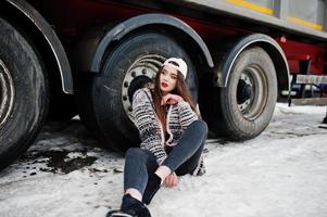 bruna ragazza casual elegante in berretto seduto contro le ruote del camion. foto