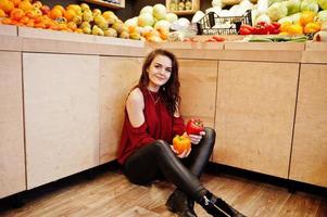 ragazza in rosso che tiene due peperoni sul negozio di frutta. foto