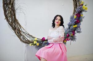 giovane ragazza bruna in gonna rosa e camicetta bianca posata all'interno contro una grande corona decorata. foto