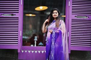 ragazza indù indiana al tradizionale saree viola poste in strada contro le finestre viola. foto