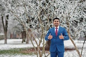 elegante modello indiano uomo alla moda in abito posato al giorno d'inverno mostra i pollici in su. foto