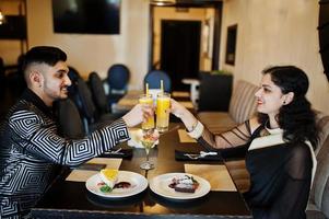 adorabile coppia indiana innamorata, indossata a saree e abito elegante, seduta al ristorante e applausi insieme dal succo d'arancia. foto