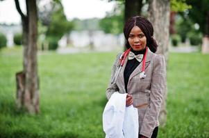 la giovane dottoressa afroamericana tiene il camice bianco a portata di mano con uno stetoscopio posato all'aperto. foto