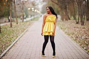 elegante donna afroamericana in abito giallo in posa contro il parco autunnale. foto